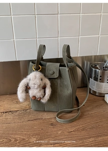 Detalle del bolso de cuero verde oscuro con costuras blancas y colgante de conejo de peluche