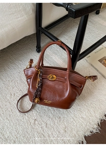 Detail of vintage brown leather bucket bag with gold oval lock and woven key charm