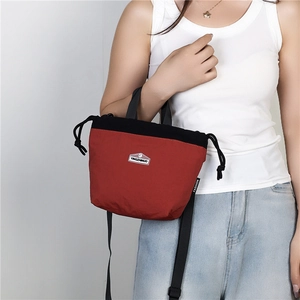 Red and black nylon drawstring crossbody bag shown on model with shoulder strap
