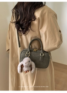 Detail view of dark grey Boston bag with textured finish, gold hardware and plush rabbit charm