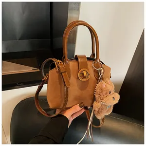 Detail der braunen Wildledertasche mit goldenem Drehverschluss und Plüsch-Hundeanhänger