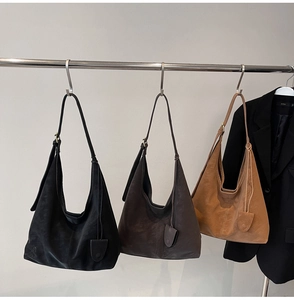 Three minimalist hobo tote bags in black, dark brown, and caramel suede displayed on racks