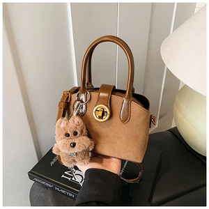 Detail einer braunen Wildlederhandtasche mit Glattledergriff und süßem Welpenanhänger