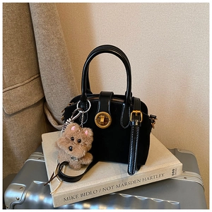 Detail einer matt schwarzen Wildlederhandtasche mit goldener Schnalle und Plüschtier