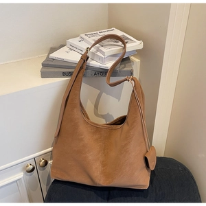 Detail view of a brown leather hobo bag with vertical stitching and mini coin purse charm