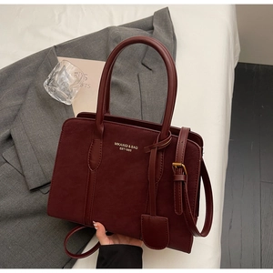 Detailansicht der burgunderroten Ledertasche mit Goldaufschrift auf weißem Bettzeug