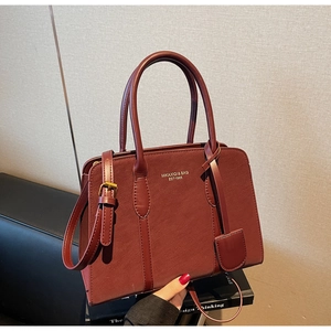 Detailansicht der burgunderroten Ledertasche mit Goldlogo und strukturierter Oberfläche