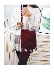 Detail view of dark red suede crossbody bucket bag featuring long tassel fringe accents