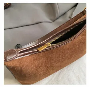 Close-up of golden zipper hardware on brown suede and croc-embossed baguette bag