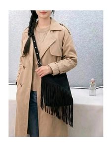 Detail of a black suede fringe bucket bag worn with a beige trench coat on a model