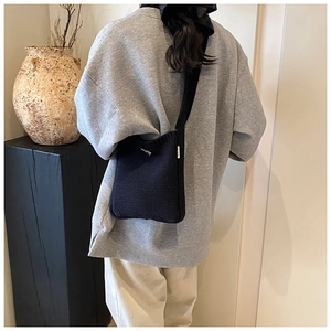 Détail d'un sac seau en tricot noir avec fine bandoulière sur une tenue décontractée