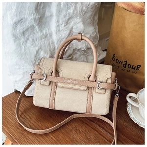 Detail van beige suède handtas met bruine lederen bies en glanzende zilveren metalen details