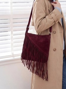 Vintage burgundy suede bucket bag with stylish tassels shown on a trench coat model