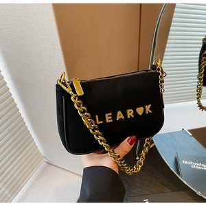 Close-up of black matte suede shoulder bag with gold chain strap and metal logo lettering