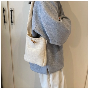 Détail du sac seau en maille crème montrant le tissage vertical et le bouton en bois