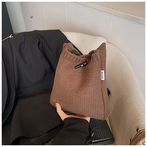 Détail d'un sac seau en tricot marron foncé avec bouton en bois et étiquette logo MISS