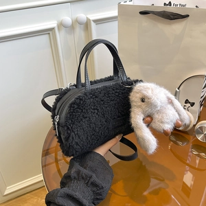 Detail of black faux fur mini handbag featuring a cylinder shape and a cute bunny charm