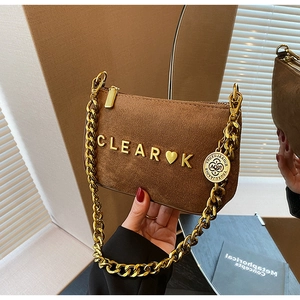 Detailed close-up of brown suede baguette bag with gold heart logo and chunky chain strap