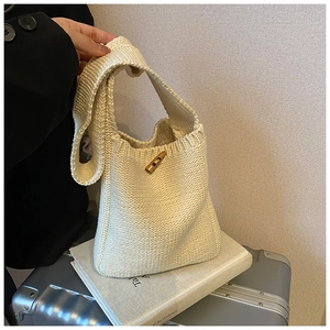 Détail du sac seau en maille crème montrant la texture tissée et le bouton en bois