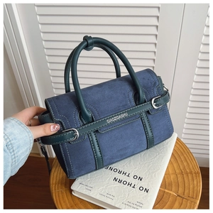 Detail van blauwe suède en donkergroene leren handtas met logo op houten standaard