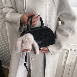 Detail of plush black faux shearling bag with fashion label and beige bunny charm