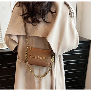 Brown suede crossbody bag with gold chain strap and heart logo shown on model