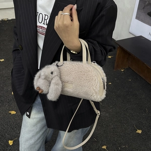 Detail view of beige plush crossbody bag with cute bunny pendant and leather shoulder strap