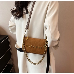 Detailed close-up of brown suede crossbody bag with gold chain and CLEAR metal logo