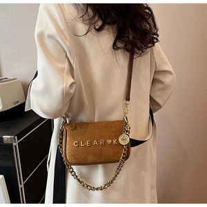 Detail of brown suede shoulder bag with gold chain and metal logo on the front