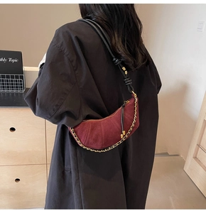 Detail van bordeauxrode suède halve maan tas met gouden ketting en leren franjes