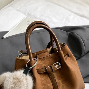 Detail shot of brown matte leather bucket bag with top handles and plush ball charm