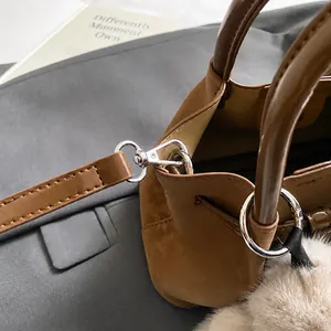 Detail of a brown suede bucket bag featuring a silver metal hook and plush ball charm
