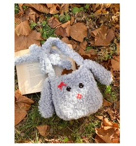 Dettaglio borsa a tracolla con coniglio in peluche grigio, fiocco rosso e naso a quadri
