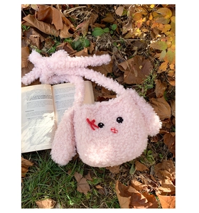 Dettaglio borsa a tracolla in peluche rosa con viso di animale su foglie autunnali