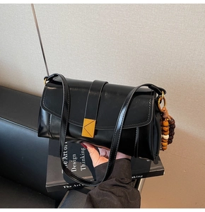 Detail of black glossy leather shoulder bag with gold metal buckle and wooden beads