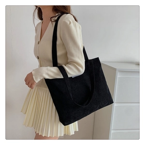 Detail of black corduroy tote bag showing ribbed texture and minimalist white logo tag