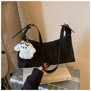Détail du sac dumpling noir en cuir avec plis doux et un pendentif de chiot en peluche