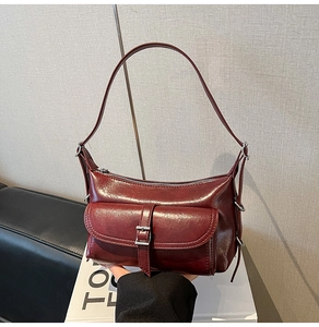 Detailed view of burgundy glossy leather shoulder bag featuring a front pocket with silver buckle
