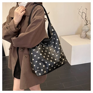 Détail d'un sac cabas punk noir à clous argentés porté à l'épaule par un mannequin