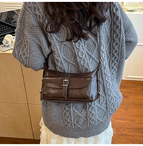Detailed view of deep brown faux leather pillow bag with silver buckle and textured surface
