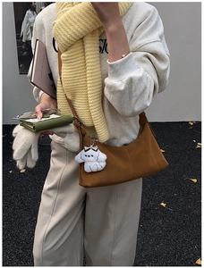 Détail d'un sac hobo marron avec coutures verticales et breloque chien en peluche