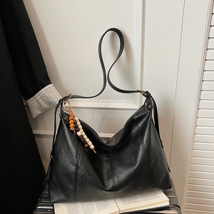 Detail of a black leather tote bag featuring a decorative wooden bead tassel accent