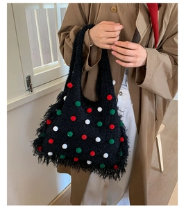 Detail einer schwarzen Stricktasche mit bunten Pompons und Fransen getragen von Model