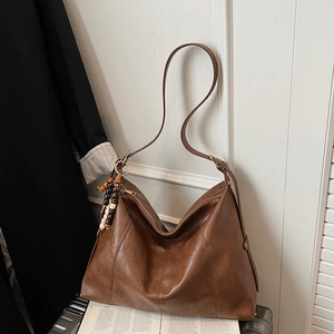 Detail of dark brown leather hobo bag with vintage wooden bead charm and seam stitching
