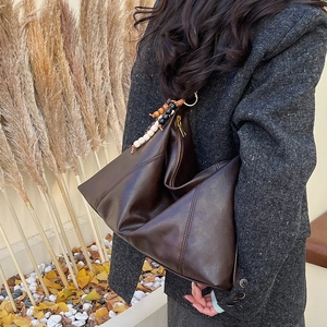 Detail of deep brown PU leather shoulder bag with decorative bead charms and stitching