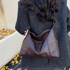 Close-up of deep brown glossy leather tote bag with vertical stitching and bead charm
