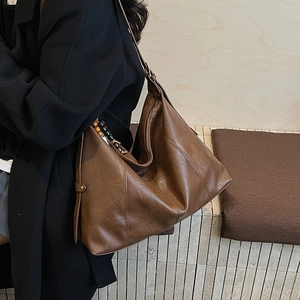 Detail of a large brown shoulder bag featuring leather stitching and colorful beaded strap