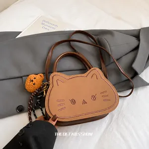 Dettaglio della borsa a mano a forma di gatto in pelle marrone con ciondolo a orso
