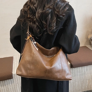Close-up of brown faux leather tote bag with stylish wooden bead pendant and stitching