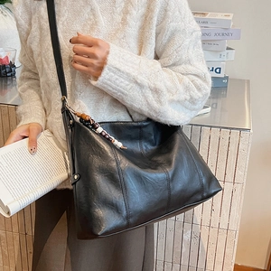 Detail of a black leather tote bag featuring vertical stitching and a beaded tassel charm